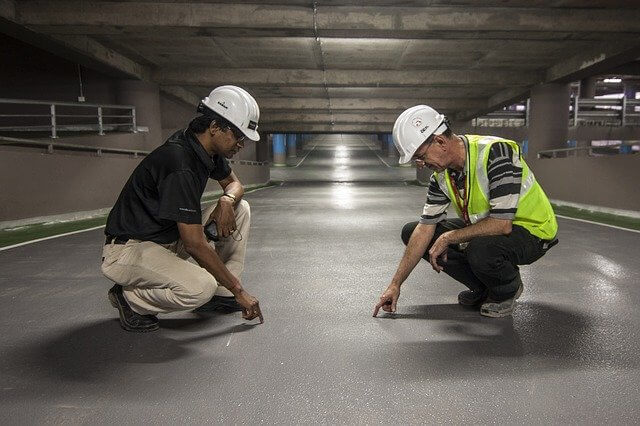 Two construction workers inspecting the floor in a parking garage.