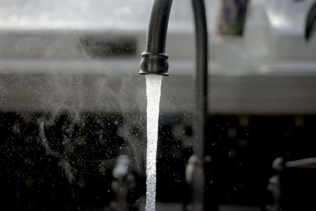 Water flowing from a kitchen faucet with splashing droplets visible in the air.
