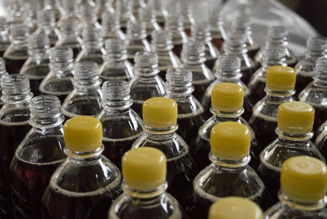 Rader av flaskor med gula lock som innehåller en mörk vätska.